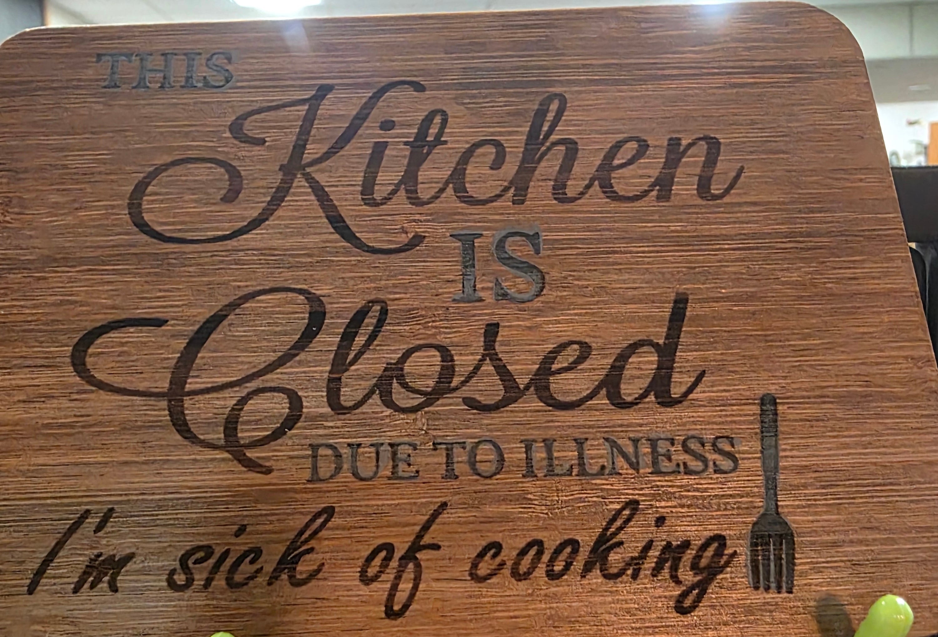 Wooden sign with humorous text about a closed kitchen due to illness, hanging on a wall.