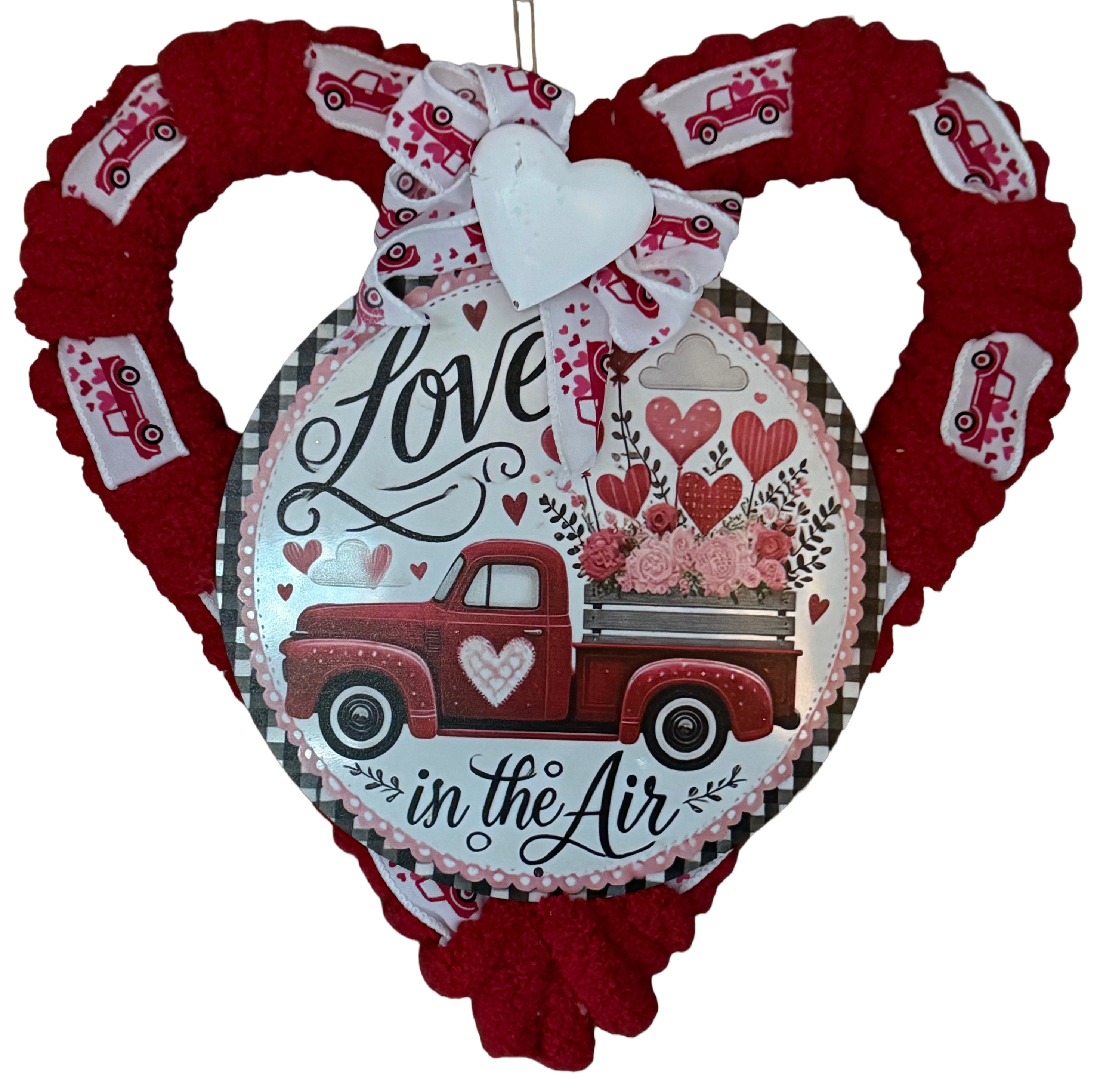 Heart-shaped wreath with a red truck and 'Love is in the Air' text, surrounded by smaller hearts and ribbons.